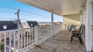 Une terrasse en bois avec une balustrade blanche, donnant sur une plage où se trouvent des maisons et une ligne électrique.