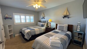 A bedroom with two beds, a ceiling fan, a window with blinds, and nautical-themed decor. - 341 El Matador (Fort Walton Beach)