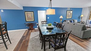 A dining area with a glass table, dark chairs, and a blue accent wall. - Yacht Club 2-404 (North Myrtle Beach)