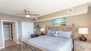 A bedroom with a bed, bedside tables, a ceiling fan, a painting, and a closet. - Yacht Club 1-1103 (North Myrtle Beach)