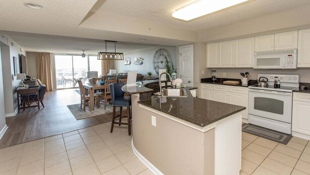A modern kitchen with white cabinets, a central island, and a dining area with a table and chairs. - Yacht Club 1-1103 (North Myrtle Beach)