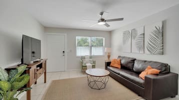 A living room with a sofa, coffee table, TV, and a ceiling fan.