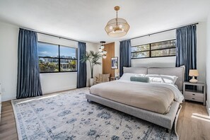 Une chambre avec un grand lit, une table de chevet, une lampe et une vue sur l’extérieur.