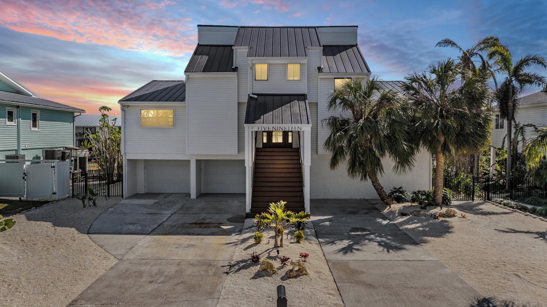 A modern two-story house with a dark roof, a central entrance with a wooden door, and a driveway leading to a garage.