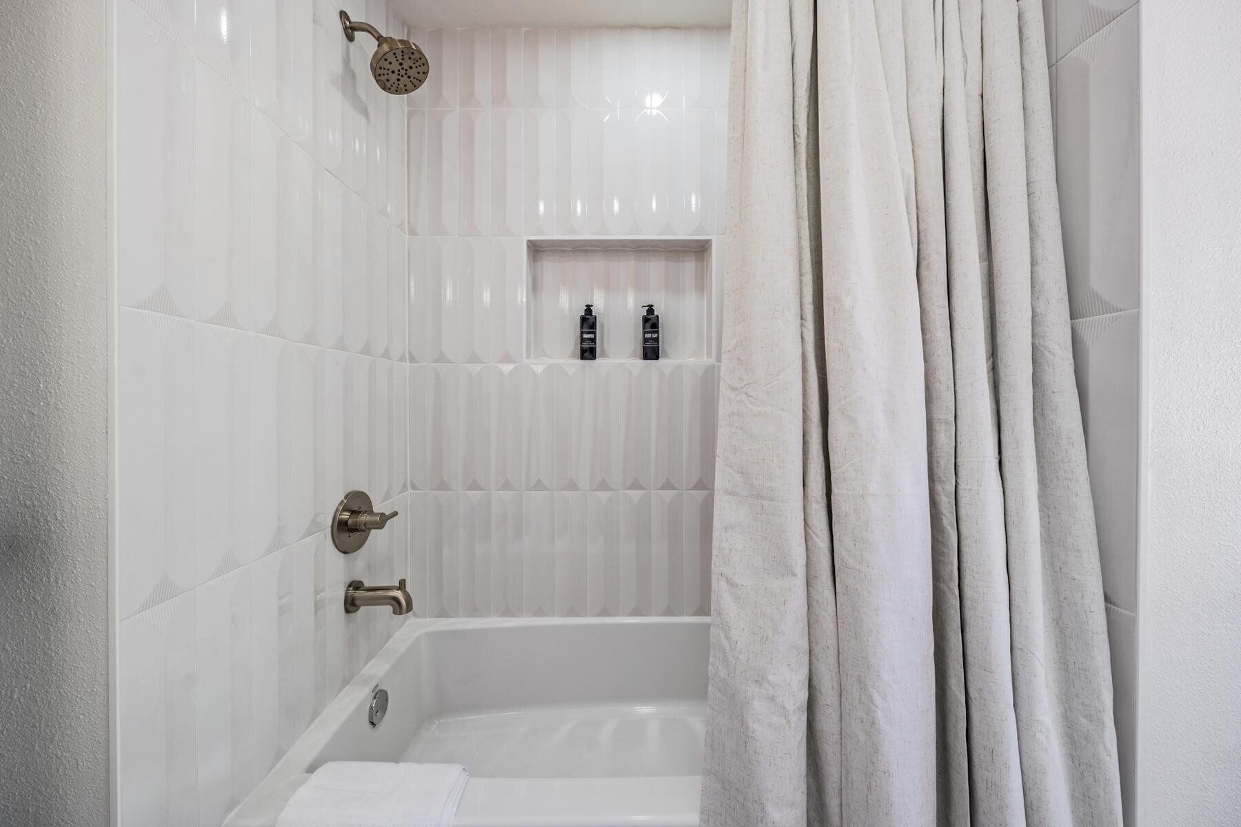 A bathroom with a bathtub, a showerhead, and a shelf with toiletries.