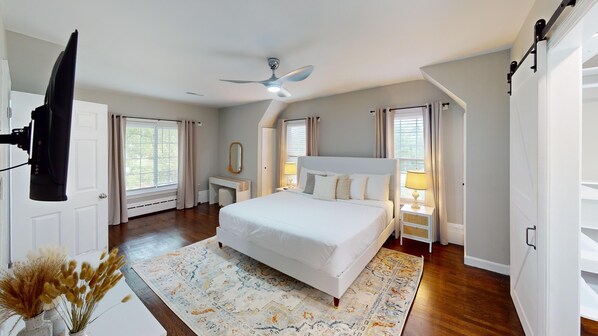 Une chambre à coucher avec un grand lit, un ventilateur de plafond, une table de chevet avec une lampe et une fenêtre avec des rideaux.