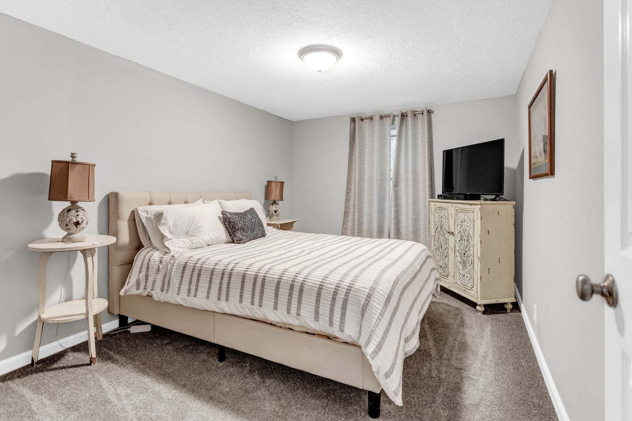 A bedroom with a bed, two bedside lamps, a television, a cabinet, and a door.