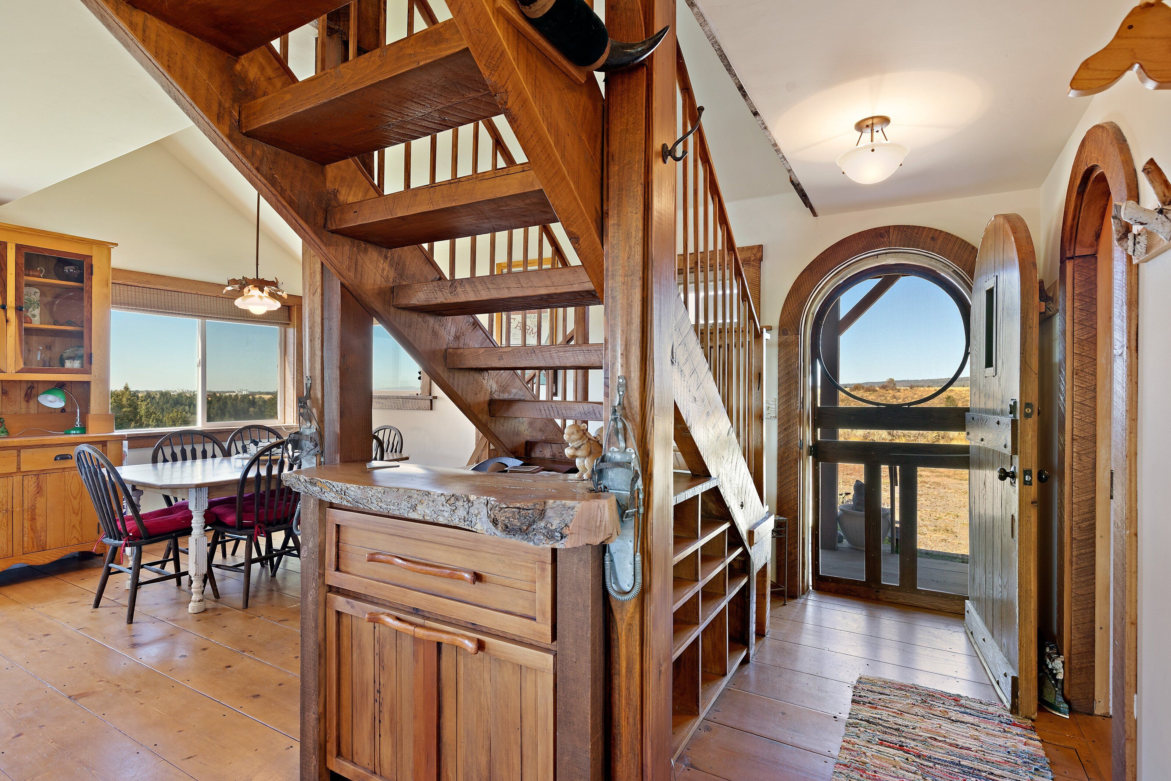 A wooden staircase leading to a second floor, a dining area with a table and chairs, and a large arched doorway.