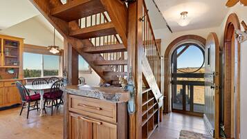 A wooden staircase leading to a second floor, a dining area with a table and chairs, and a large arched doorway.