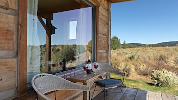 A wooden deck with wicker chairs and a table, a bottle of wine, and glasses on the table.