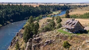 A rustic cabin with a deck overlooking a river and forest.