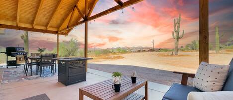 A covered outdoor seating area with a wooden table, chairs, and a sofa.