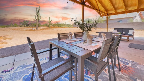 An outdoor patio with a wooden table and chairs, a cactus in the background, and a sunset view. - Boulder Apache Junction (Apache Junction)
