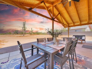 Een terras buiten met een houten tafel en stoelen, een cactus op de achtergrond en een uitzicht op de ondergaande zon.