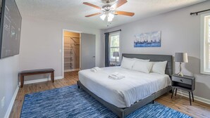 A bedroom with a bed, a ceiling fan, a nightstand, a lamp, a painting, and a walk-in closet. - Save Midweek 3Br Near Lake Acworth and Downtown (Acworth)