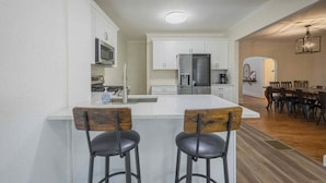 A modern kitchen with white cabinets, a stainless steel refrigerator, and a bar area with two stools. - Five Points Mill House (Athens)