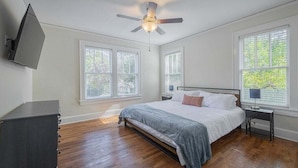 A bedroom with a bed, a ceiling fan, a TV mounted on the wall, and a window with blinds. - Five Points Mill House (Athens)