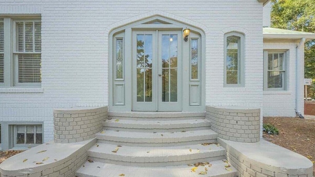 A white building with a central entrance featuring a set of steps leading up to a door with glass panels. - Five Points Mill House (Athens)
