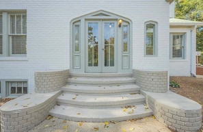 A white building with a central entrance featuring a set of steps leading up to a door with glass panels and a small lamp above it. - Five Points Mill House (Athens)