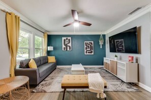 A living room with a sofa, ottoman, coffee table, TV, and artwork on the wall. - Rare Exclusive Retreat Private Hot Tub King Bed (Arlington)