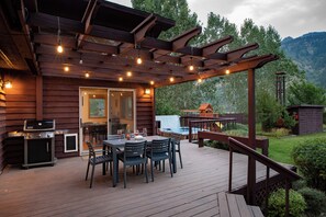 Una terraza de madera con pérgola, mobiliario exterior y una parrilla.
