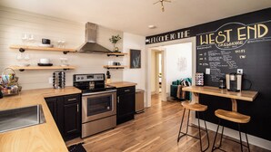 Een moderne keuken met houten planken, een zwart en roestvrijstalen fornuis en een prikbord met de tekst 'WELCOME TO THE WEST END BREWHOUSE'.