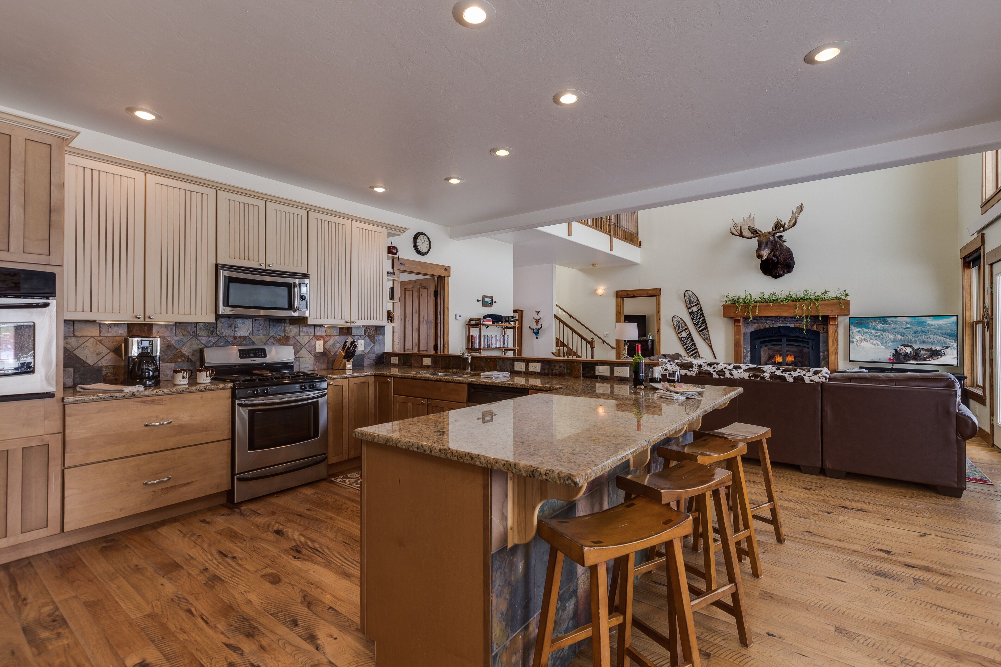 A spacious kitchen with wooden cabinets, a large island with stools, a microwave, a stove, and a fireplace.