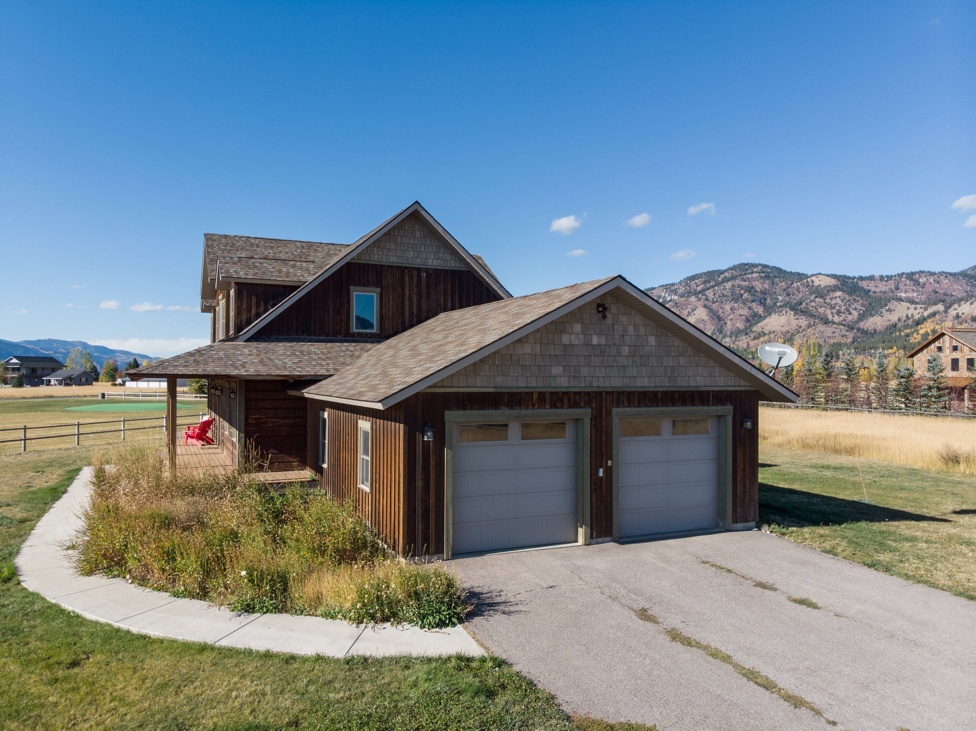 Une maison en bois à deux étages, dotée d’un garage, d’un porche couvert et offrant une vue sur les montagnes en arrière-plan.