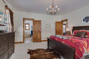 Ein Schlafzimmer mit Bett, Schminktisch, einer Kronleuchter und einer Kuh auf dem Boden.