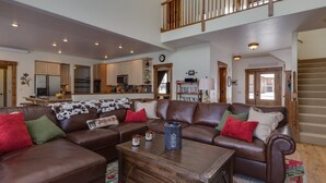 Ein geräumiges Wohnzimmer mit einer braunen Ledersofa, einem Holztisch und einer Küche im Hintergrund.