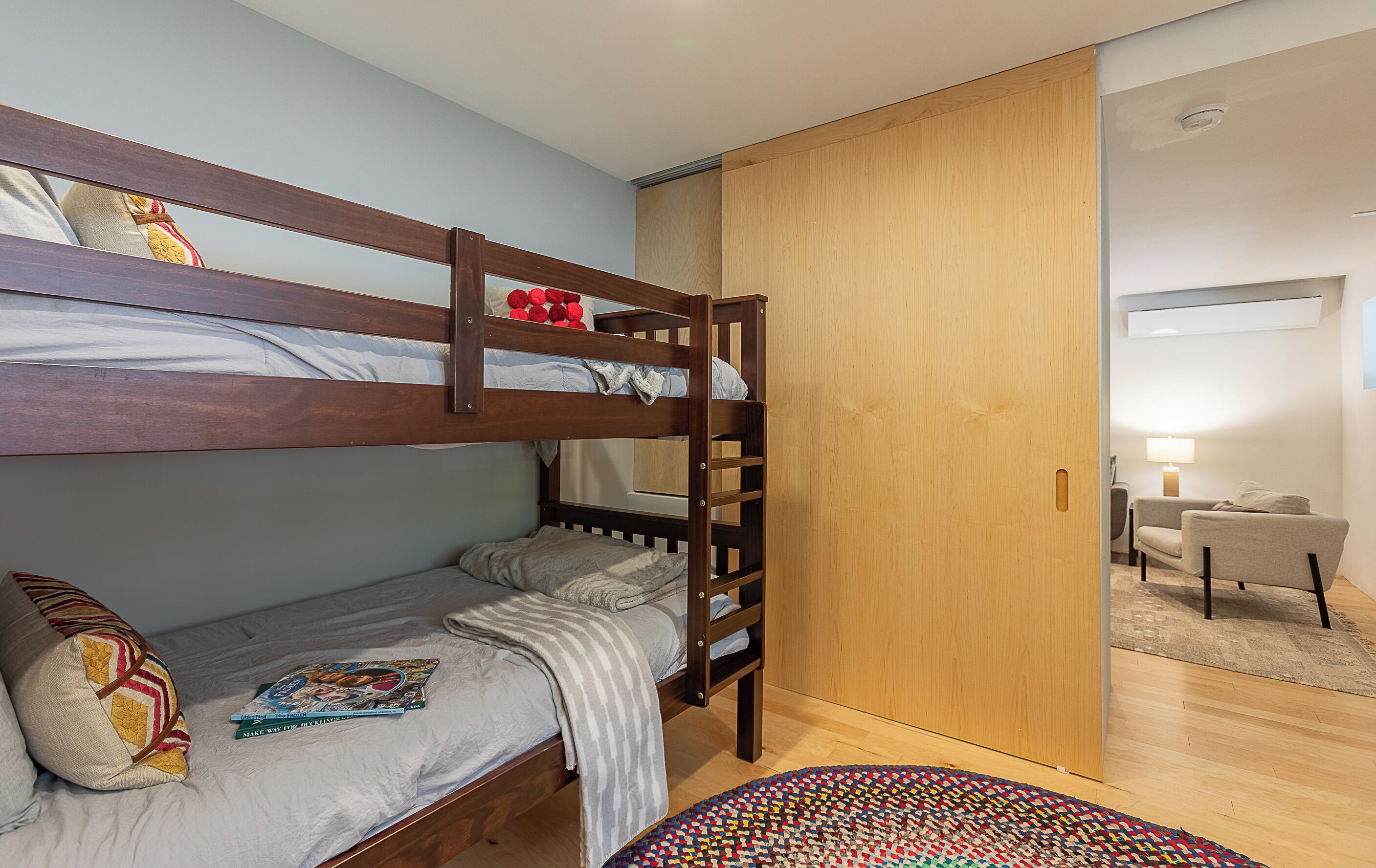 Une chambre avec un lit superposé, une échelle en bois, un petit bureau et une chaise.