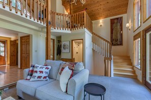 A spacious living area with a high wooden ceiling, a staircase, and a large window. - Alpine Breakwater (Alpine)