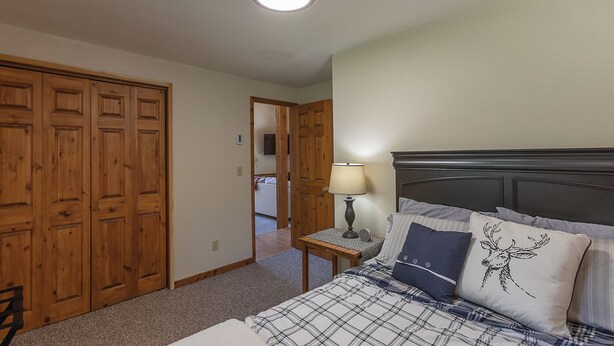A bedroom with a bed, a nightstand, a lamp, and a closet. - Alpine Breakwater (Alpine)