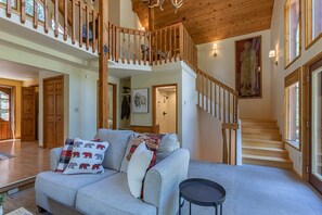 A spacious living area with a grey sofa, wooden staircase, and large windows. - Alpine Breakwater (Alpine)