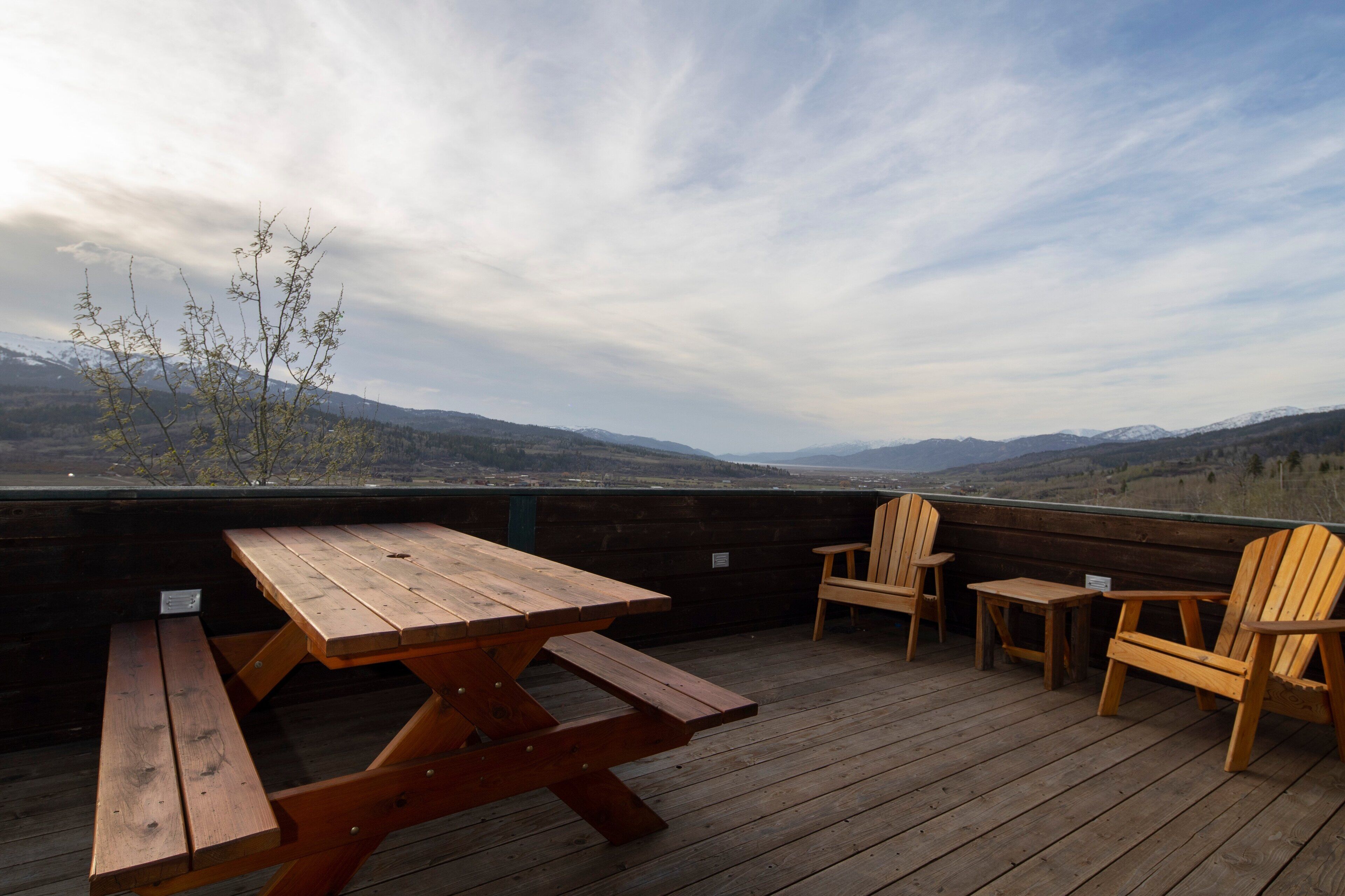 A wooden deck with picnic tables and chairs, overlooking a mountainous landscape.