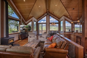 A spacious living room with a high ceiling, large windows, a fireplace, leather sofas, and a dining area. - Alpine Recharge (Alpine)