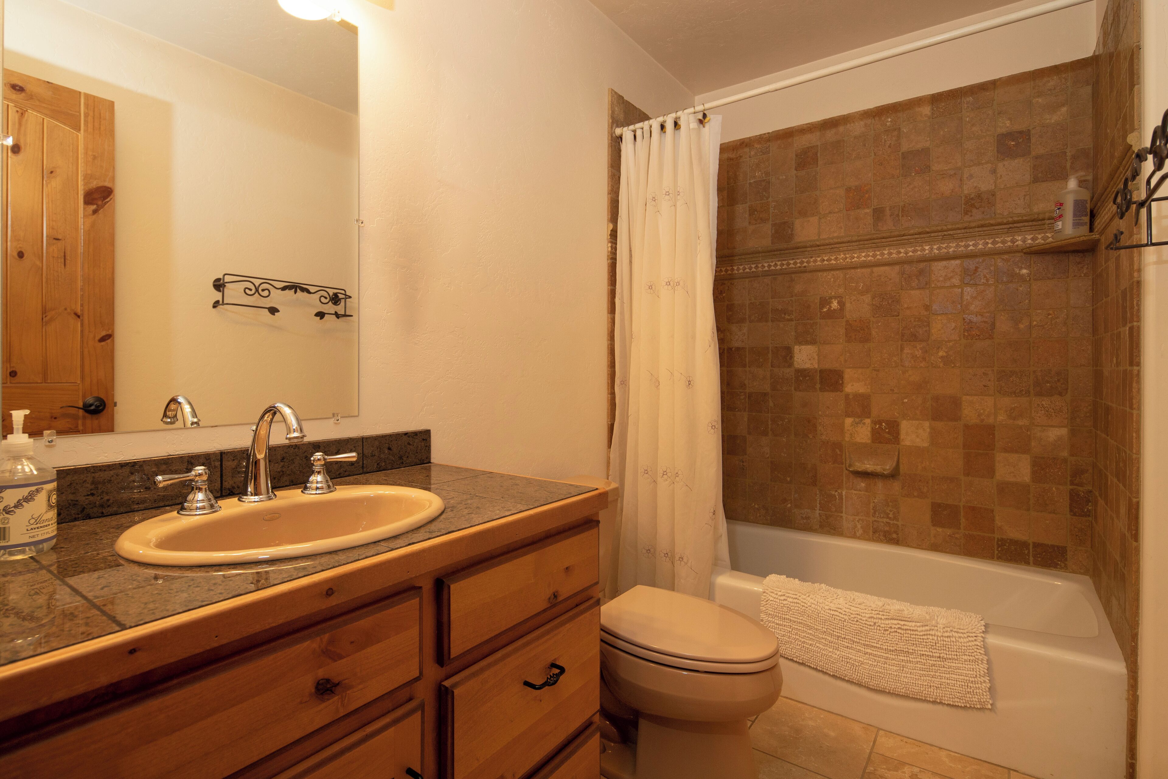 A bathroom with a sink, mirror, wooden vanity, toilet, and a shower area with a tiled wall.