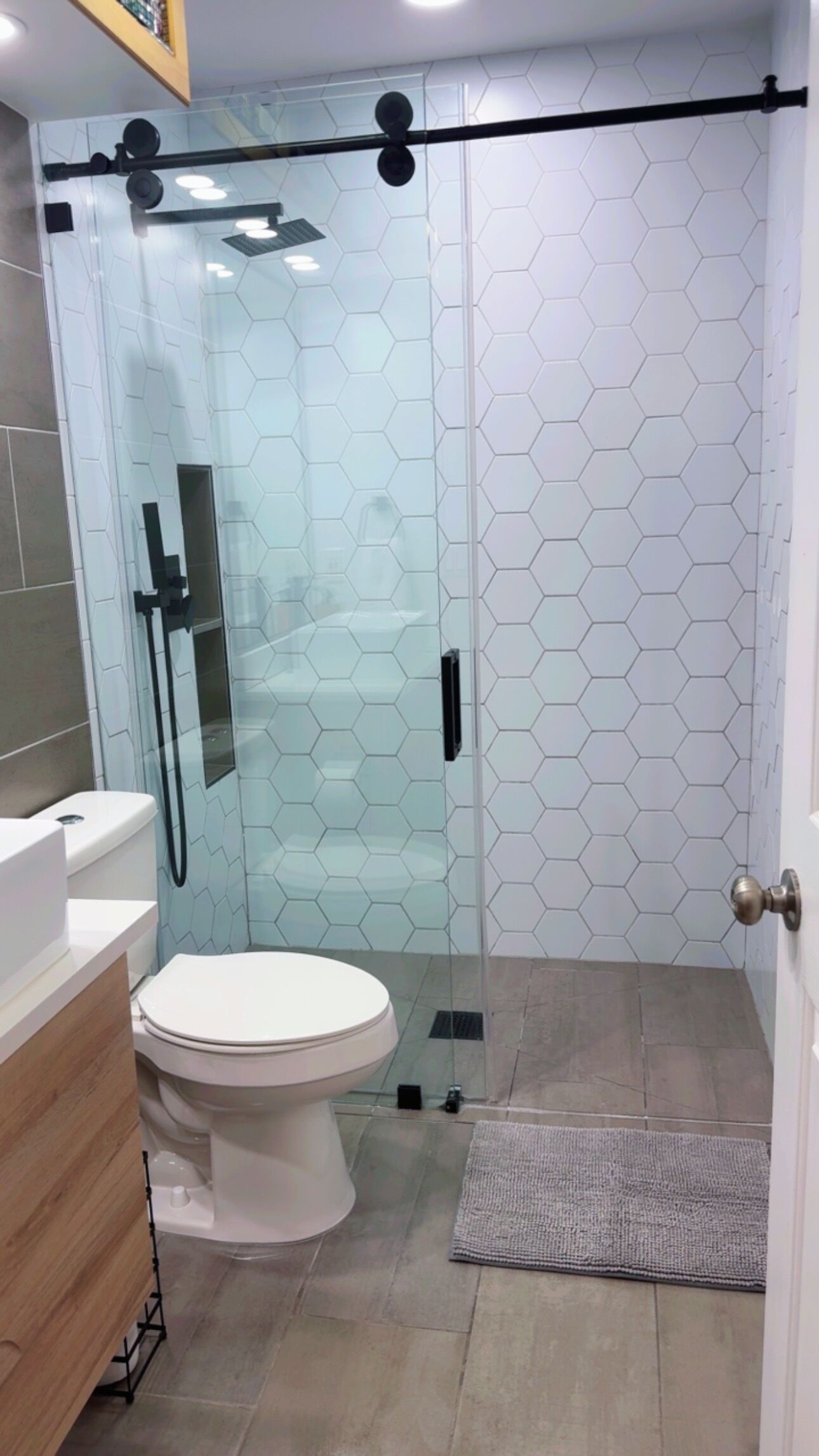 A modern bathroom with a glass-enclosed shower, a white toilet, and a wooden vanity.
