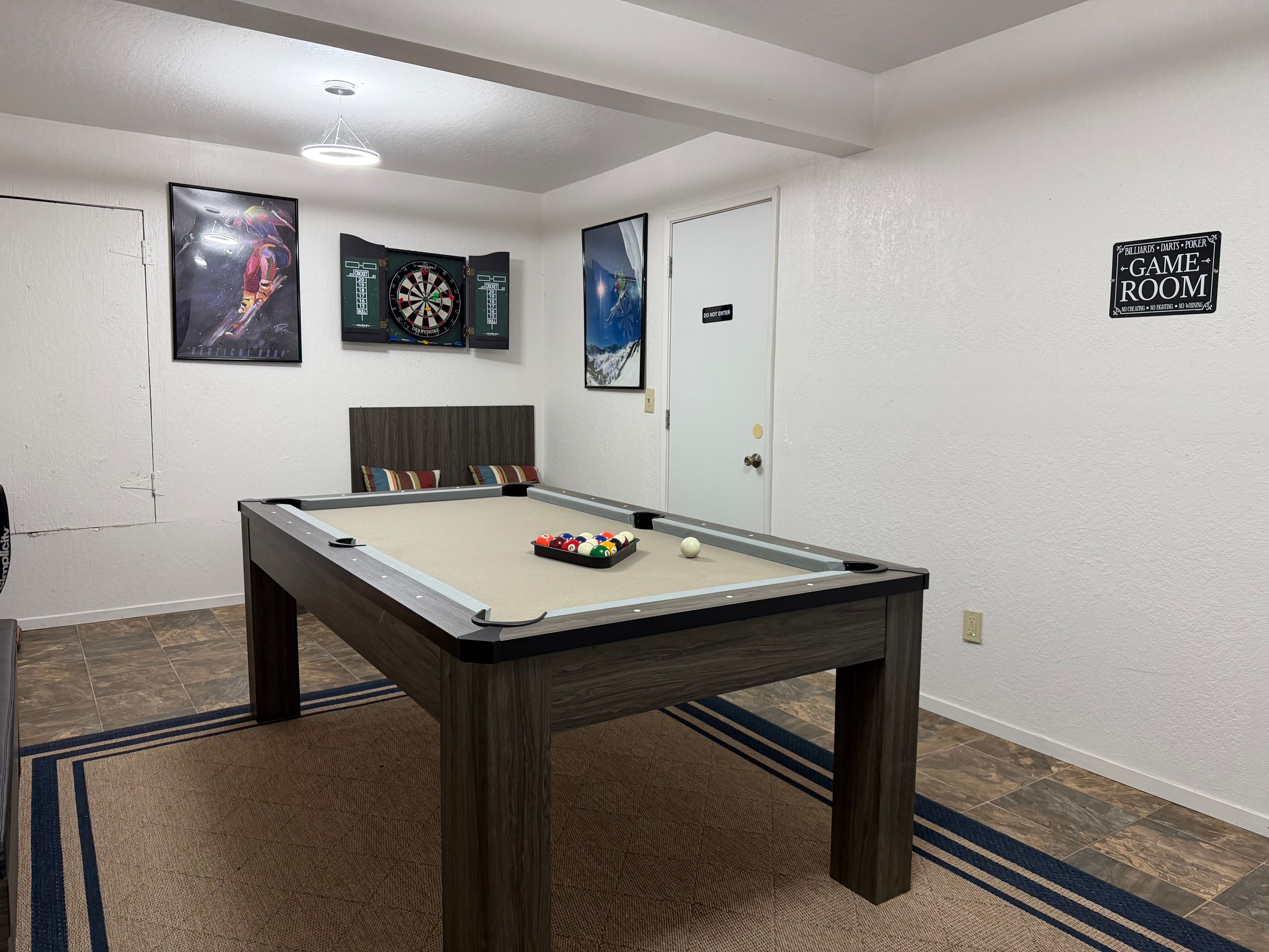 Ein Billardtisch mit Kugeln, eine Dartscheibe und ein Schild mit der Aufschrift 'GAME ROOM'.