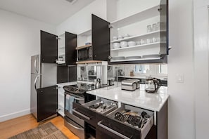 A modern kitchen with a built-in microwave, toaster, and kettle, along with a refrigerator and oven. - Standish House by BCA Furnished Apartments Standish House (Atlanta)