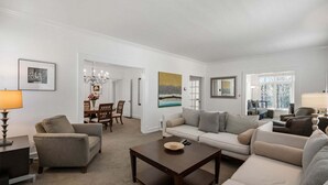 A living room with a sofa, armchairs, a coffee table, and a dining area with chairs and a chandelier. - Standish House by BCA Furnished Apartments Standish House (Atlanta)