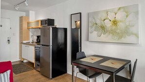 Eine kleine Küche mit Kühlschrank, Mikrowelle und Backofen, ein Esstisch mit Stühlen und ein großes Blumenbild an der Wand.