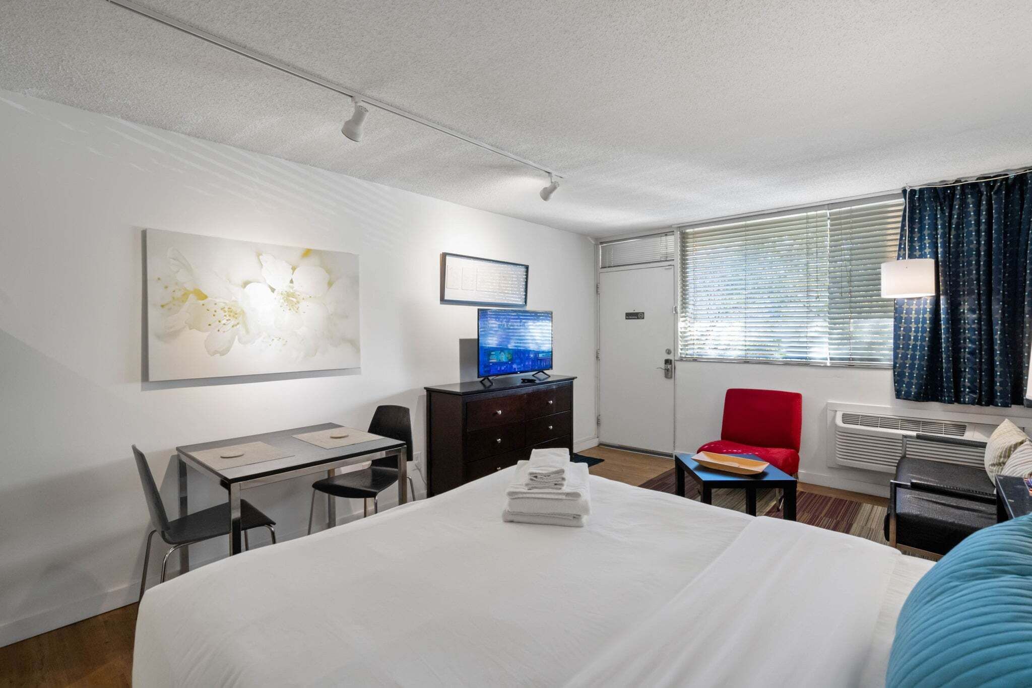 Une chambre d’hôtel avec un lit, un bureau, une chaise, une télévision et un fauteuil rouge.