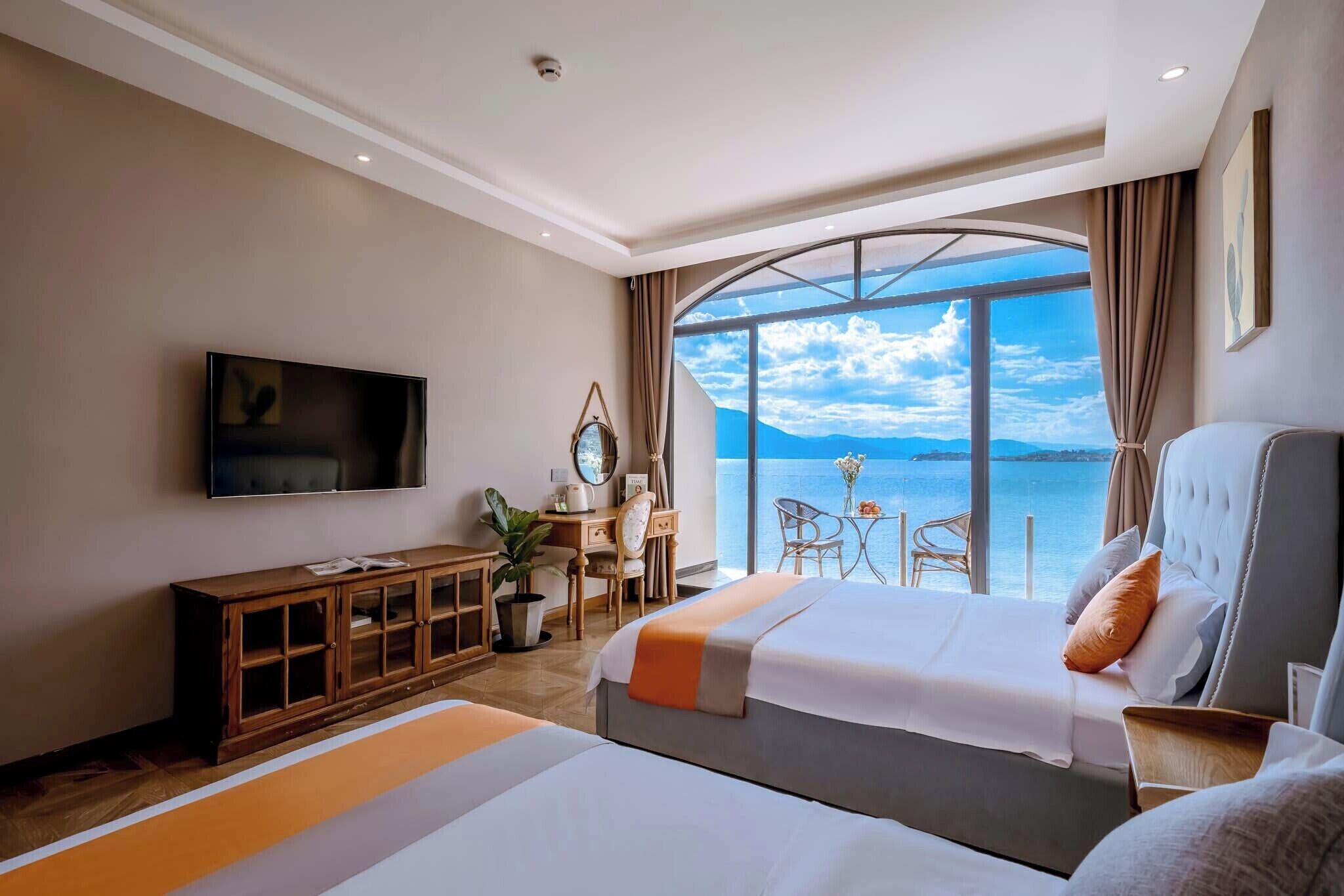 Un cuarto de hotel con un ventanal amplio que ofrece vistas al mar, una cama, un escritorio con una silla y un televisor montado en la pared.