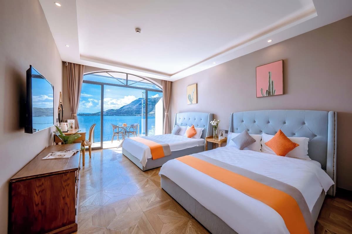 A hotel room with two beds, a TV, a desk, and a large window offering a scenic view.