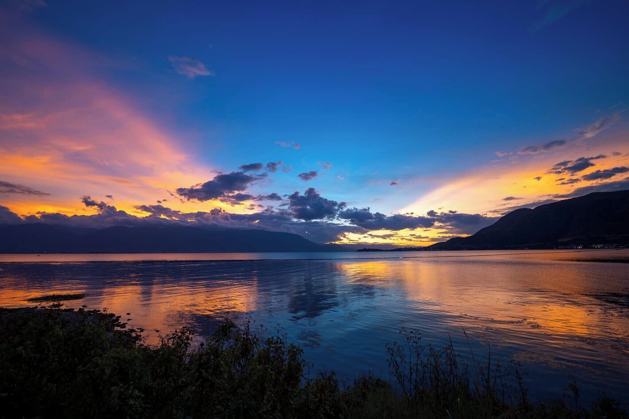 A calm lake at sunset with mountains in the background.