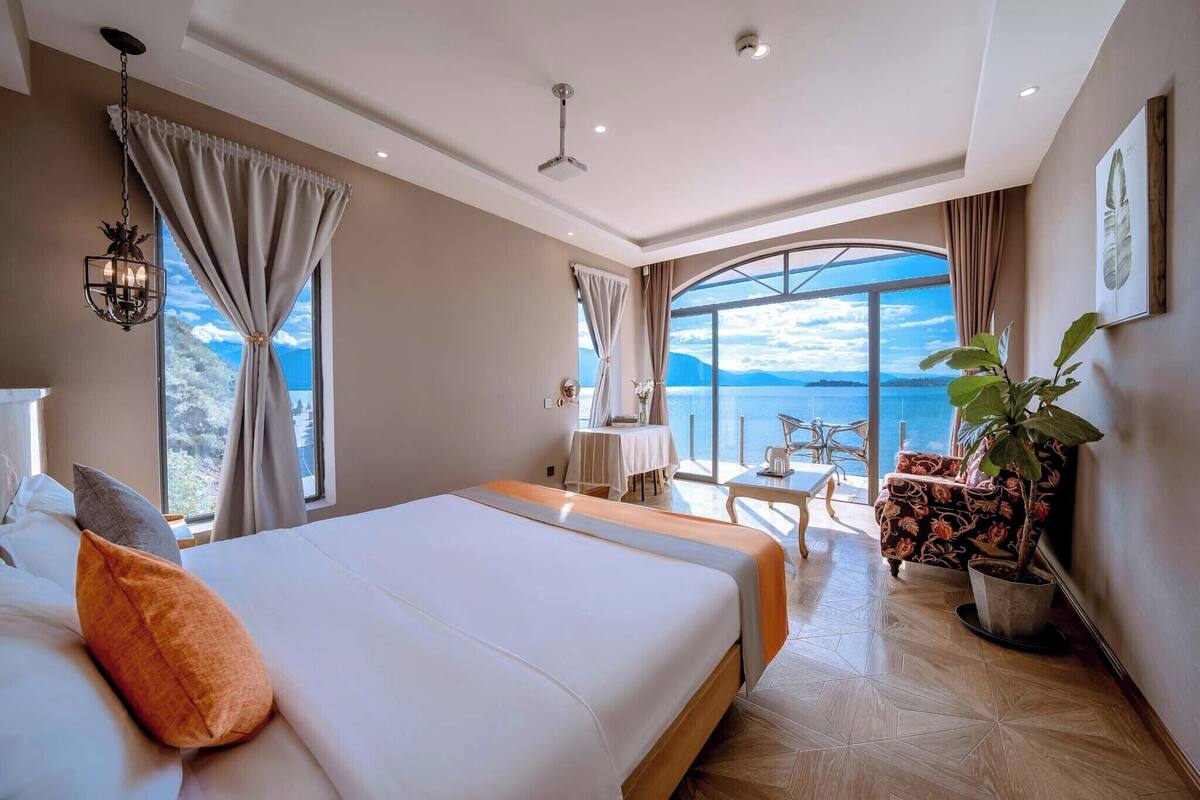 A hotel room with a large bed, a dining area, and a view of the sea.