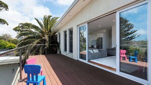 Een modern huis met een terras, grote schuifpuien en een woonkamer met een bank en fauteuils.