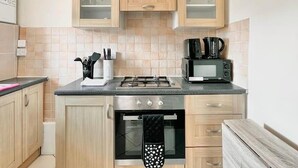 Une cuisine compacte dotée de meubles en bois, d’une cuisinière à gaz, d’un four à micro-ondes et d’un four encastré.