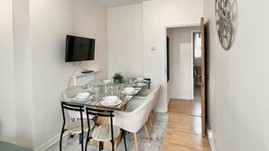 Un espace repas moderne avec une longue table dressée pour six personnes, un téléviseur à écran plat fixé au mur et une pièce décorative en métal accrochée au mur.